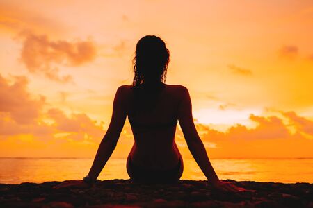 Woman silhouette sitting against sunset on the beachの写真素材