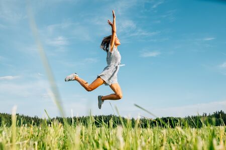 Happy woman jumping in green field against blue sky. Summer vacation conceptの写真素材