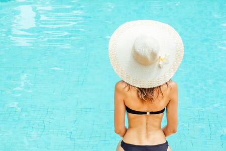 Back view of woman in swimsuit and hat which sitting near the pool