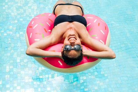 Enjoying suntan woman in black bikini on the inflatable mattress in the swimming pool. Summer...