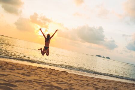 Silhouette of happy joyful woman jumping and having fun at the beach against the sunset. Freedom and vacation conceptの写真素材