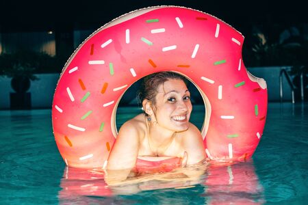Beautiful young woman with inflatable ring in hotel pool at nightの写真素材