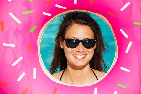 Beautiful young woman with inflatable donut in blue swimming pool