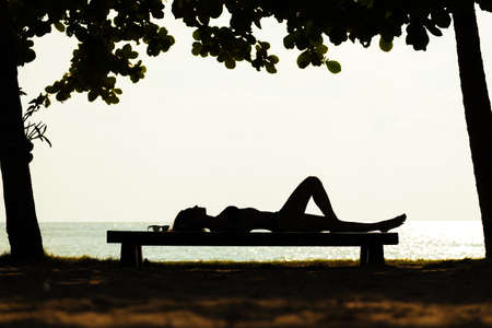 Silhouette of attractive young woman in bikini lying on the bench near the seaの写真素材