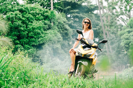 Young beautiful woman riding scooter on the road with palm trees. Tropical travel concept