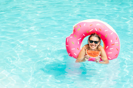 Happy woman wearing sunglasses with red watermelon enjoy in swimming pool with pink rubber ring