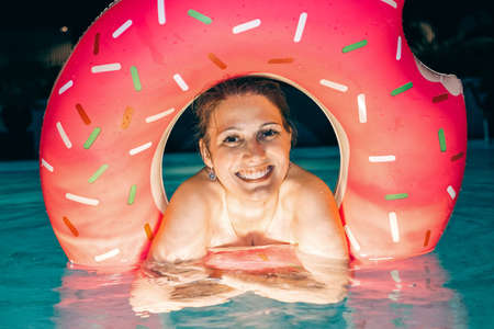 Beautiful woman with inflatable ring in hotel pool at nightの写真素材