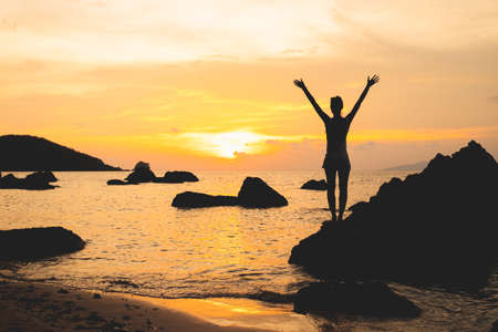 Lady's silhouette with raised arms against calm sunset beach