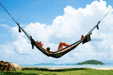 Summer vacations concept. Happy woman in black bikini relaxing in hammock on tropical beachの写真素材