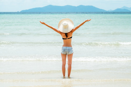 Rear view of a beautiful brunette young girl with raised hands, looking at ocean. Freedom conceptの写真素材