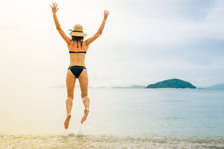Happy young woman jumping on the beach. Back viewの写真素材