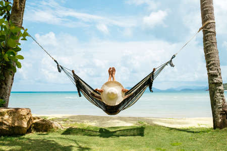 Summer vacations concept. Happy woman in black bikini relaxing in hammock on tropical beachの写真素材