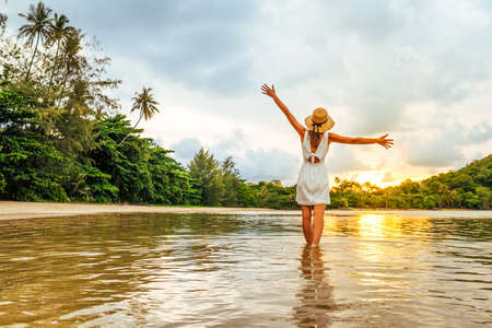 Young happy woman rising hands up enjoying beautiful sunset on the seaの写真素材