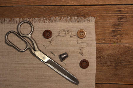 Scissors, buttons, thimble and needle on linen cloth on a wooden board background