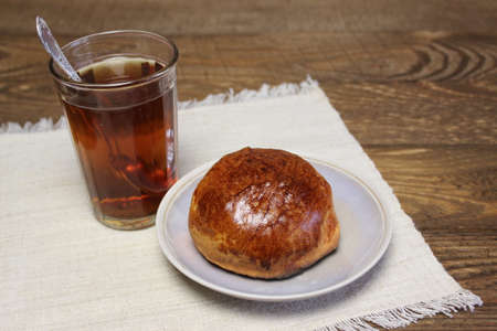 Glass of tea and a bun on a wooden board background