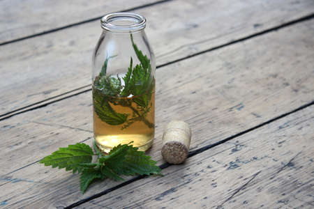 Jar with alcohol tincture and nettle leaves on a background of boards.の写真素材