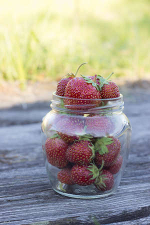 Red ripe strawberries in glass jar on the background of wooden boardsの写真素材