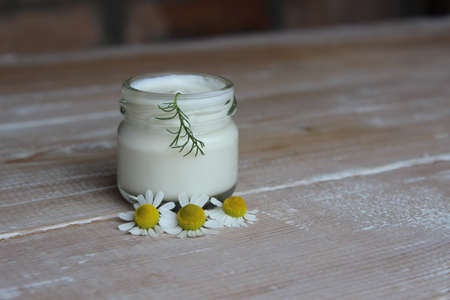 Organic cream with white chamomile flowers on background of boardsの写真素材