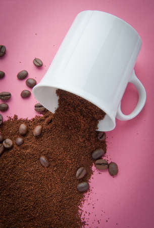 cup with coffee grind and coffee beans spilled on a pink backgroundの写真素材