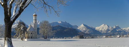 panorama view in bavaria, germany, with famous church St. Coloman to the alps mountains at sunny winter dayの写真素材