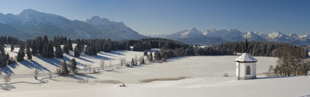 panorama view in bavaria, germany, with a little chapel to the alps mountains at sunny winter dayの写真素材