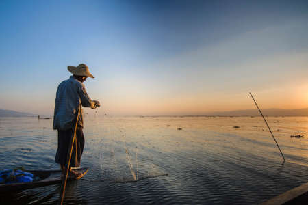 A local fisherman is fishing by boat in unique style. By using his feet to control the boat on famous lake on December 25, 2013 in Inle, Myanmar.のeditorial素材