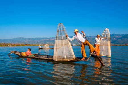 The local fishermen are fishing by boat in unique style. By using their feet to control the boat on famous lake on December 25, 2013 in Inle, Myanmar.のeditorial素材