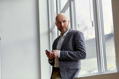 Bald Businessman Standing With a Mobile in His Handsの写真素材