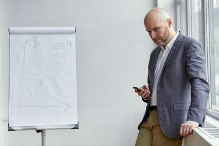 Bald Businessman Standing With a Mobile in His Handsの写真素材