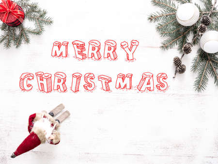 merry christmas red inscription, view from above, next to a Christmas tree branch with bubbles and a gift and santa claus on slingsの写真素材