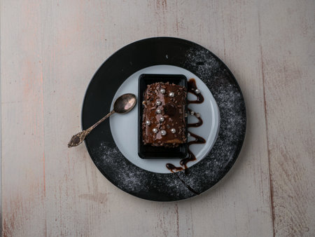 cake with chocolate cream on a plate decorated with a teaspoon next to it, a view from above, wooden bright background, warm atmosphere. place for textの写真素材