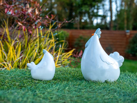 white porcelain hens on green grass, blurry garden in the backgroundの写真素材
