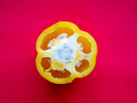 yellow pepper cross-section with visible seeds, on a red background, top viewの写真素材