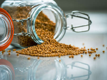 Dry mustard seeds in a glass bottle and a pile of mustard on a white background. Close-up macro