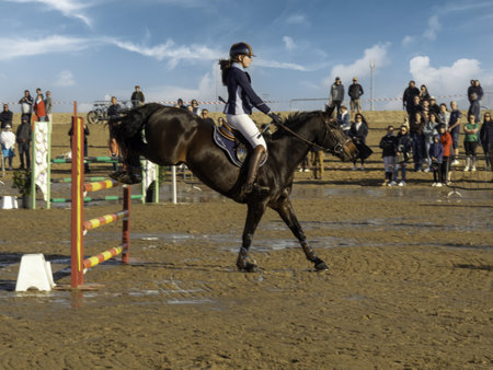 Ouistreham, France, April 2022. A school show jumping at The Ridge on a beach in Normandy. Young woman jockey on horseback is jumping over a hurdle.のeditorial素材