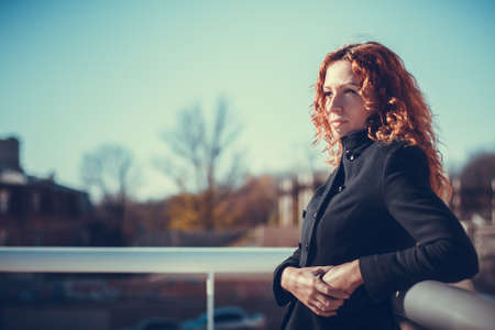 Cute girl with red hair standing against the blue sky backgroundの写真素材