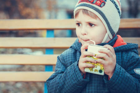 autumn portrait little boy thinks and drinking juice a tubeの写真素材