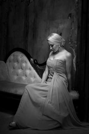 Sexy blonde woman in long pink dress sitting on the couch. Black and white retro style photoの写真素材