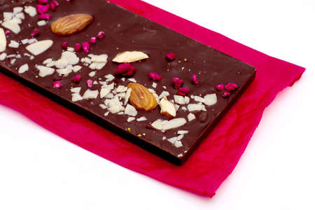 Handmade white, milk and dark chocolate bar with a variety of dried fruit and nut toppings on a red...