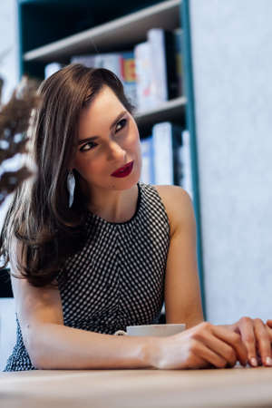 beautiful girl in a cafe at a table drinks coffee smiling at someone against