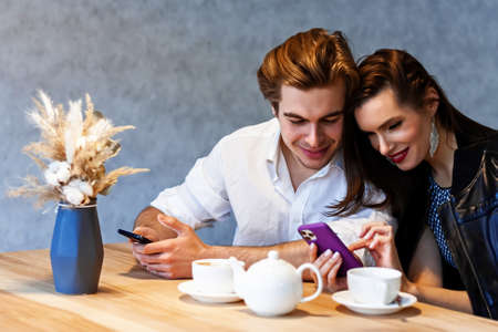 beautiful couple in a cafe at a table drinks coffee and watching something on her phone