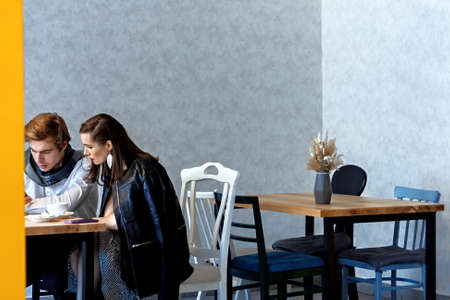 beautiful couple in a cafe at a table drinks coffee and watching something on his phoneの写真素材