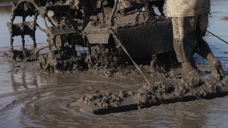 A close up of a peasant man taming soil of a field with agricultural machinery equipment. Splashes...