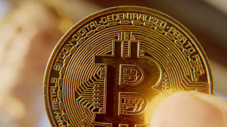 A young happy crypto entrepreneur in a white shirt smiles from happiness in the rays of sunlight holding a golden bitcoin in his hand.の写真素材