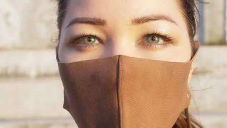 Close-up of a mixed-race girl with beautiful green eyes and a medical mask looking directly into the camera. a serious look of a young girl against the background of a sunny concrete stadium.の写真素材