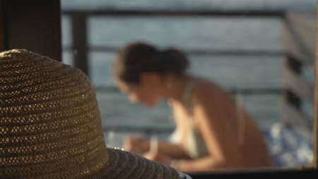 Close-up of a cute straw hat on the background of an artists girl painting a picture on a lake pier...