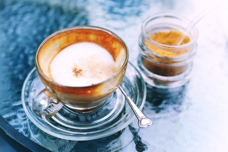 Hot coffee and sugar on glass table, Close up coffee with milk on top, selective focus, free space for text and toned image.の写真素材