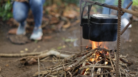 Cooking food on the campfire in the forest. The small pots on fire at camping place. Selective focus.の写真素材