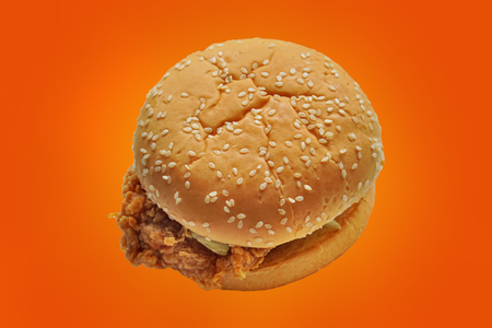 Hamburger with fried chicken on colourful background with path. Crispy chicken burger on orange background. Selective focus and free space for text. Unhealthy fast food concept.の写真素材