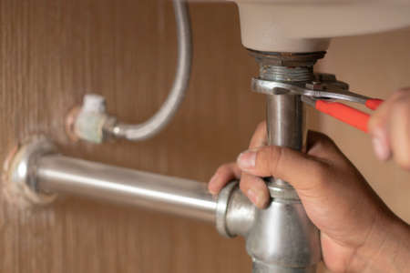Plumber repairs and maintains chrome siphon under the washbasin in bathroom. Maintanance home ideas concept. Selective focus and freespace for background.の写真素材